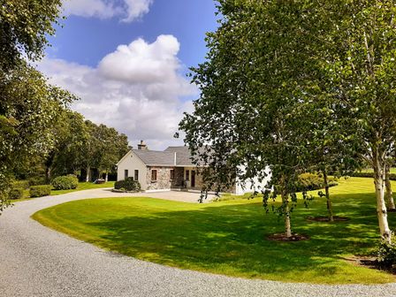 A house with a stone and white exterior surrounded by trees and a curved gravel driveway at Fraoch Cottage in Garrykennedy County Tipperary