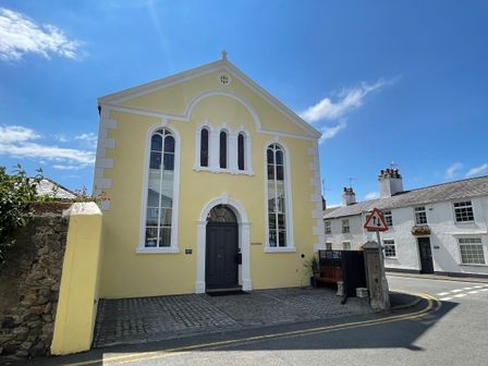 A yellow building with arched windows and a dark door next to a street with a traffic sign at Ty Biwmares in Beaumaris