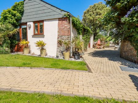 An outdoor area with a paved pathway grass potted plants a bench and trees at Cameo Atlantic Highway near Bude
