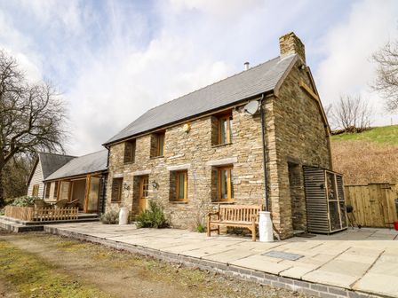 A stone house with wooden windows and doors with a bench outside and patio area at The Orchard in Llangunllo near Knighton