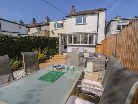 A backyard patio with a glass table and chairs next to a house at Penrallt in Cemaes Bay