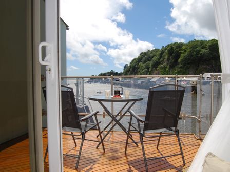 A balcony with two chairs and a round table overlooking a river and trees at The Moorings in Porthmadog
