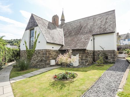 A stone and white plaster house with a steep roof and small garden with pathways at The Old School in Conwy