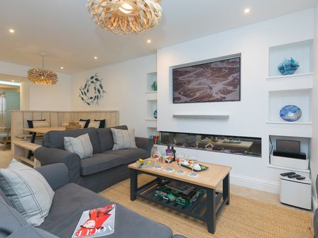 A living room with grey sofas a wooden coffee table and a mounted television above a fireplace at Pebbles in St Ives