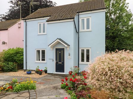 A blue two-story house with a dark door and front garden with flowers at Mews Cottage in Laugharne