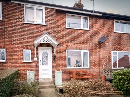 Front view of a brick house with white door and window and a wooden bench outside at The View in Whitby