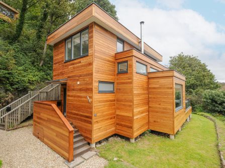 A modern wooden house with large windows surrounded by trees and grass at 9 Cedars in St Agnes