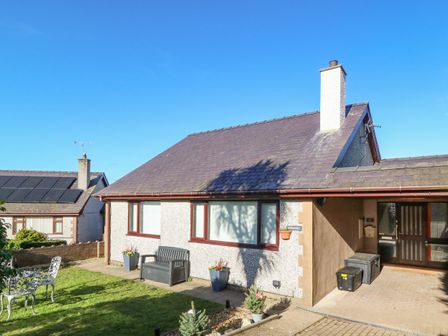 A single story house with a sloped roof and chimney a bench and potted plants in front at Normandy in Nefyn