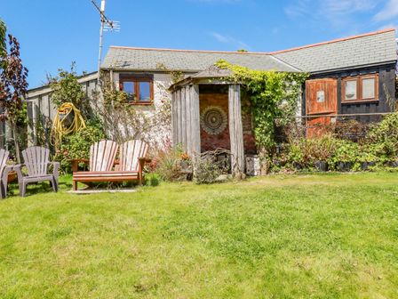 A garden with lawn chairs a wooden gazebo climbing plants and a house with a slate roof at Seashells Atlantic Highway near Bude