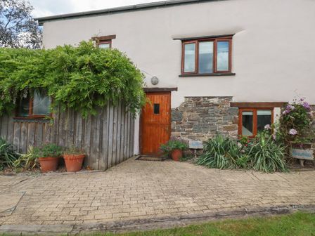 A house exterior with a wooden door and windows surrounded by plants and flowers at Oyster Atlantic Highway near Bude