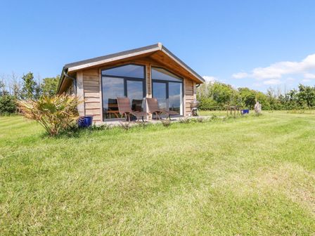 A wooden cabin with large glass doors two chairs and a barbecue on a grassy lawn at Atlantic Lodge Atlantic Highway near Bude