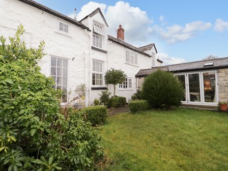 A grassy garden with shrubs and a white stone house with multiple windows and a glass door at Ty Croes in St George near Bodelwyddan