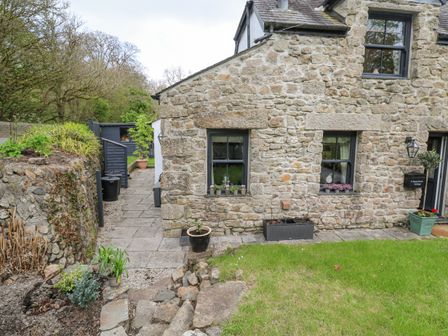 Stone cottage exterior with windows and potted plants on a grassy lawn at Wood Brook Cottage in Crowan