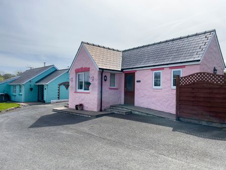 A pink house with a wooden door and windows next to a blue house with a similar design at Pen- y- Bryn @ Canllefaes in Penparc near Cardigan