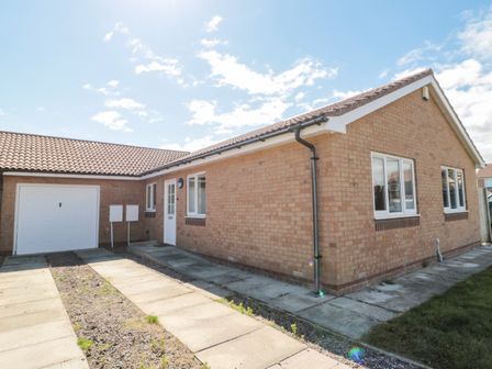 A brick bungalow with a tiled roof a driveway a garage and a paved pathway at 20 Southmead in Amble