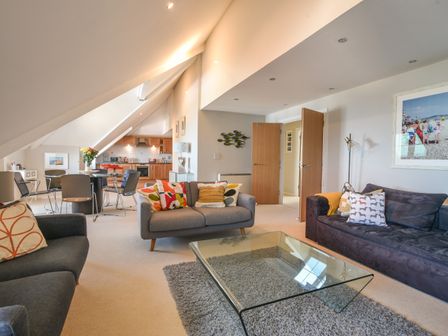 A living room with sofas pillows glass coffee table and an open kitchen at 13 Buckfields in Lyme Regis