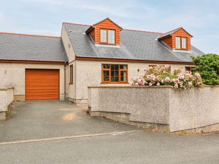 A house with a driveway garage window and flowers in front garden at Yr Hen Efail in Cemaes Bay