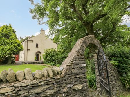 A house behind a stone wall with an arched gate and green trees at Ewedale Farm in Pennington near Ulverston