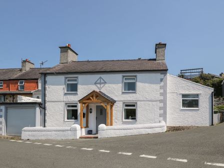 A white two-story house with a wooden porch and a garage on a corner at Royal Oak Cottage in Amlwch Port