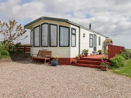 A mobile home with a wooden bench and potted flowers on a gravel driveway at The Cabin in Occumster near Lybster
