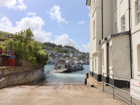 A ferry approaching a slipway between buildings with a hillside village in the background at Ferryside in Kingswear