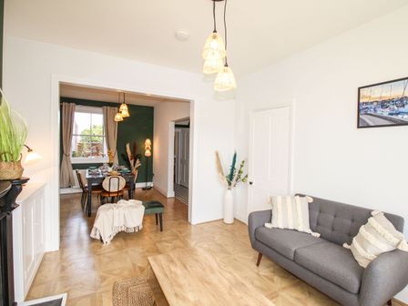 A living room with a gray sofa and wooden coffee table and a dining room with a table and chairs at Wolf Cottage in Weymouth
