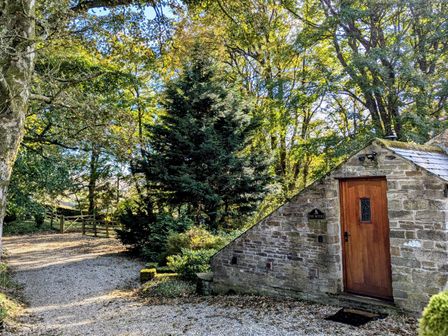 Exterior of a stone building with a wooden door surrounded by trees and a gravel path at Bothy in Nenthall near Alston