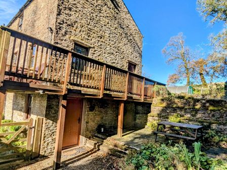 An outdoor stone patio area with a wooden picnic table and raised wooden balcony attached to a stone building at Chestnut in Nenthall near Alston