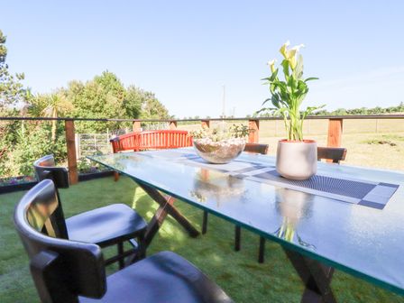 A glass outdoor table with a plant and a flower pot on a patio with chairs and a wooden bench at Atlantic Apartment Atlantic Highway near Bude