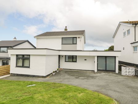 A two story house with white walls black framed windows and a driveway at Melody in Cemaes Bay