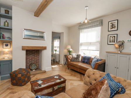 A living room with a leather sofa, wooden coffee table, and a window with blinds at Bluefin Cottage in Whitby