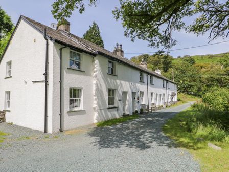 A row of white cottages beside a gravel pathway with greenery and hills in the background at Scale Force in Seatoller near Rosthwaite