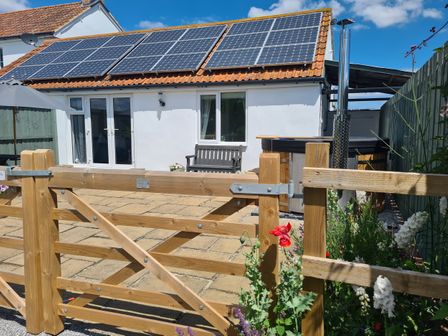 A patio area with solar panels on the roof a wooden bench a hot tub and a wooden gate at Thornhills Cottage Othery near Middlezoy