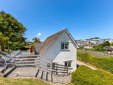 A white house with a sloped roof and surrounding greenery at Baywatch Sands in Polzeath