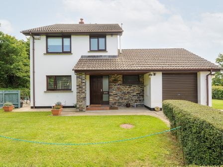 A two-story house with a tiled roof a garage door a front door and potted plants on a lawn at Spring Lodge in Eastcott near Kilkhampton