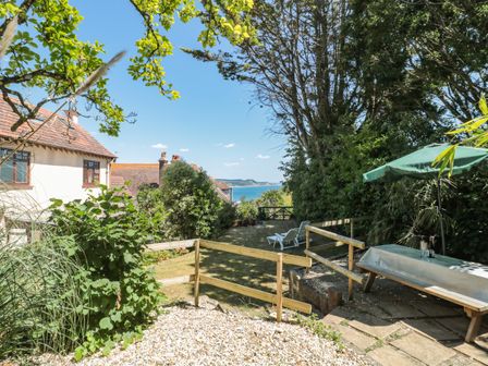 A backyard garden with a lawn chairs a picnic table with an umbrella and a view of the sea at Heselwood in Lyme Regis