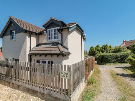 A two story house with a tiled roof and wooden fence with a slow 5mph sign on a gravel driveway at The Coach House in Lyme Regis