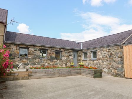 An exterior view of a stone building with multiple windows a door and flower beds at Y Beudy in Dinas near Bontnewydd