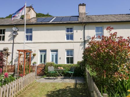 A garden with a small table and two chairs in front of a two-story house with solar panels on the roof at 7 Railway Cottages in Newby Bridge