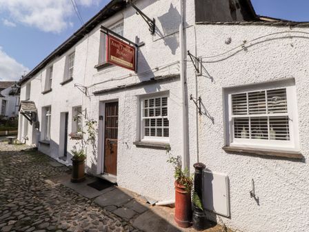 Exterior view of a white cottage with a wooden door windows and cobblestone path at Ann Tysons House Hawkshead