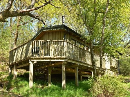 A wooden cabin with a raised deck surrounded by trees at Chapel House in Torridon