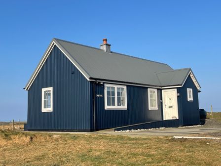 A blue house with white windows and a grey roof on a grassy area at Taigh Gorm in Baleshare near Balivanich