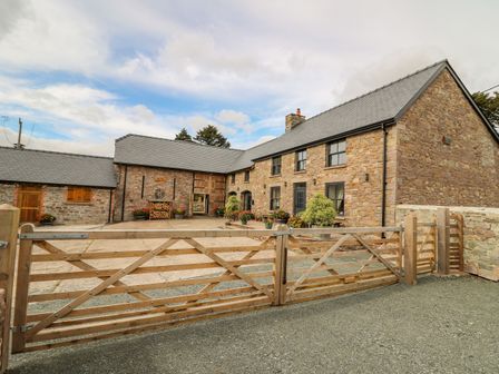 A stone farmhouse with multiple windows and a wooden gate in front at Pen Bont Home Farm Upper Chapel near Builth Wells