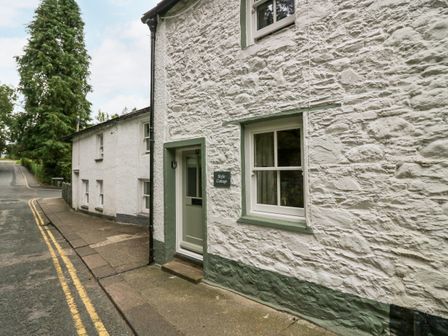 The exterior of a white stone cottage with green trim next to a paved road at Style Cottage in Keswick