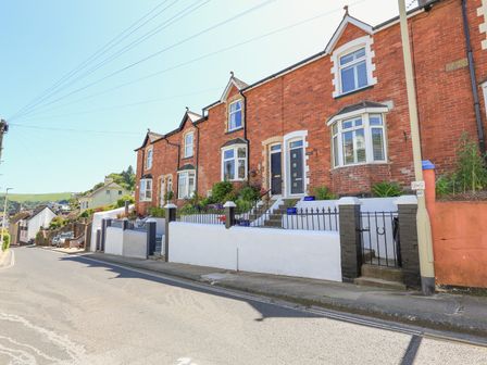 A row of brick terraced houses with front gardens and steps leading to doors on a street at Crew House in Dartmouth