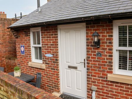 The front entrance of a brick house with a white door two windows a black outdoor light and a small table with chairs outside at Stokers Rest Whitby