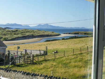 A view of grassy fields with a river flowing into the sea and mountains in the distance at Morlais Voice of the Sea in Aberffraw
