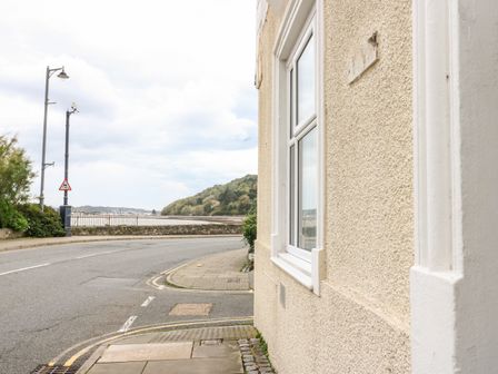 A street corner with a window on a beige textured building and a road curving toward a waterfront with trees in the background at No 62 Beaumaris