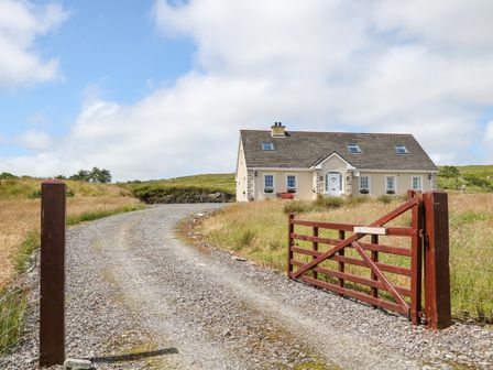 A gravel driveway leads to a house with a red gate and grassy field at Sleibhte Sliabh Liag in Carrick County Donegal