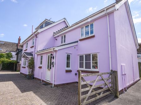 A pink two-story house with multiple windows a white door and a wooden gate in front at Seagull Cottage in Lyme Regis